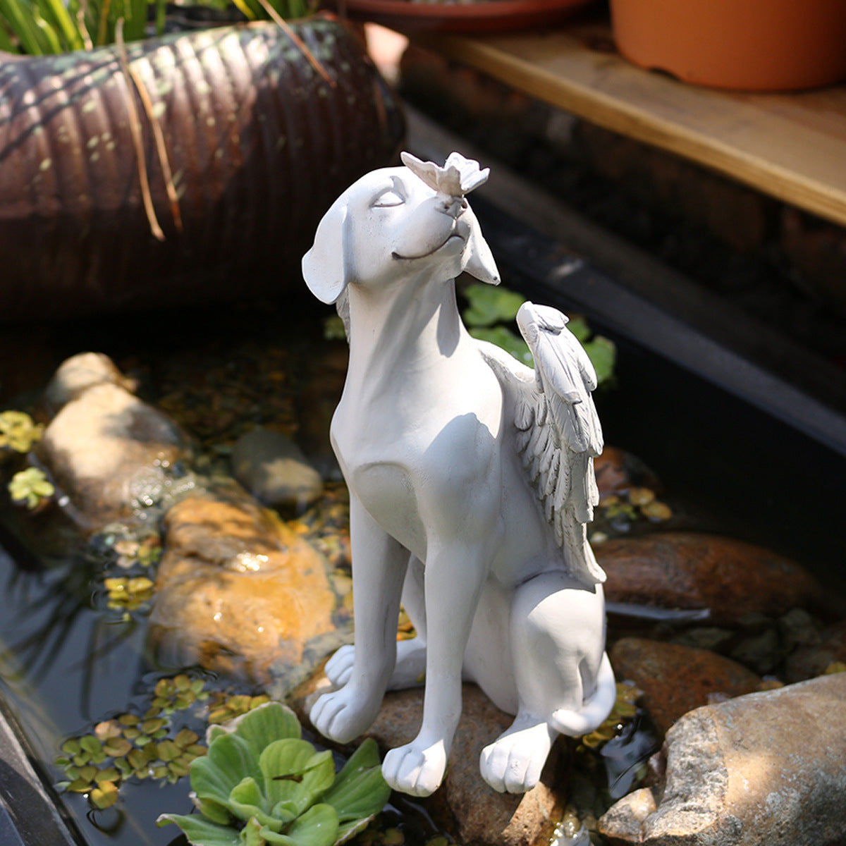 Resin angel dog memorial statue beside a garden pond